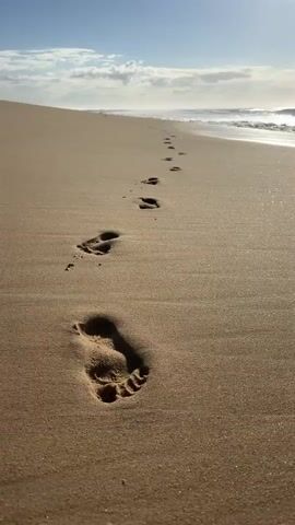 Footprints lead down a sandy beach toward the ocean. A wave washes over the footprints, erasing them from the sand.