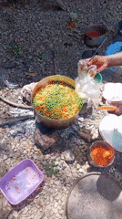 Person adds cloth to vegetable pot over outdoor fire