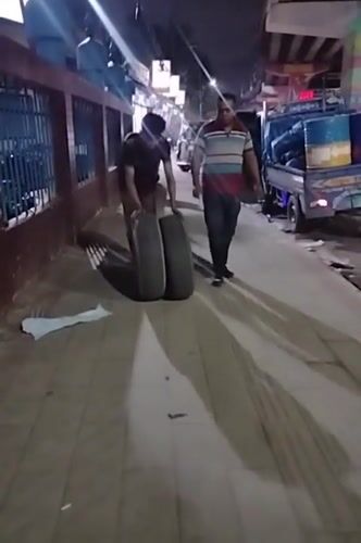Hauling large tires along a busy Dhaka sidewalk at night