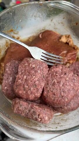 The video begins with a close-up shot of a glass bowl containing raw meat patties and what appear to be marinated pork chops, with a fork resting on top. The scene then transitions to an outdoor grill where several pork chops are cooking. The chops have prominent grill marks and are beginning to brown. The video ends with a shot focusing on the grilled pork chops.
