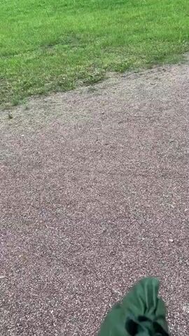 A video shows a person walking outdoors with a green umbrella. The umbrella is closed and held in the person's hand. The ground is covered with gravel. There is a grassy hill in the background. The camera is pointed downwards at the umbrella and the ground. The video appears to be shot in landscape orientation.