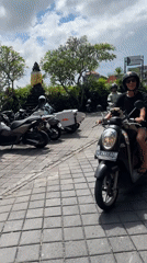 Woman rides scooter with dog through North Kuta streets