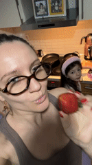 Woman eats strawberry in kitchen while child watches in Esenyurt