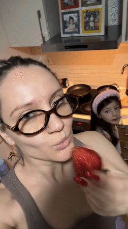 Woman eats strawberry in kitchen while child watches in Esenyurt