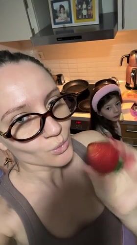 Woman eats strawberry in kitchen while child watches in Esenyurt