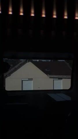 This is a video of a view from inside a train, looking out the window. The subjects are the passing scenery of suburban houses and greenery, along with some interior elements of the train carriage.

The activity is the train traveling through a residential area. We see different houses, some with red-tiled roofs and others with white facades. There are also trees and bushes, suggesting a green environment. In the foreground, parts of the train's interior are visible, including what appears to be a table and seat.

Notable details include the time of day, which seems to be daytime, possibly late afternoon or early evening, given the shadows and the warm light from the top of the frame, which could be overhead lights on the train or the setting sun filtering through. The weather appears to be clear and sunny. The location context provided is Saint-Germain-en-Laye, France, which aligns with the style of houses and fences seen. There's a sense of movement and transition as the landscape changes outside the window.

There is some visible text: graffiti on the lower left side of a building, appearing to be "GM1".