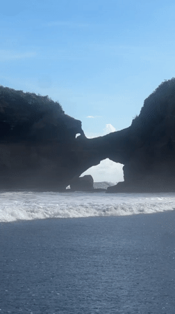 Man stands in ocean at Indonesian black sand beach