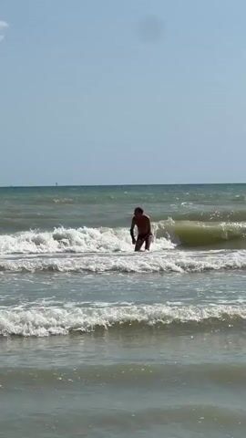 A person is in the ocean, immersed in the waves, with only their head and shoulders visible above the water. The waves are breaking around them, creating white foam. The sky is clear and blue.