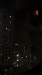 Tyumen resident cleans rainy window overlooking illuminated nighttime cityscape