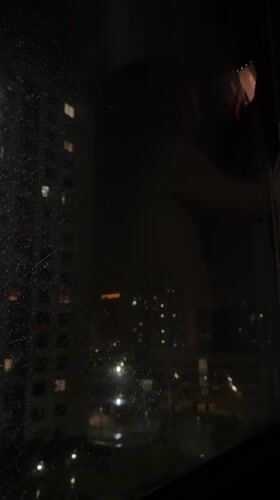Tyumen resident cleans rainy window overlooking illuminated nighttime cityscape