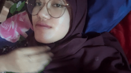 Woman in hijab photographed smiling on floral bedding