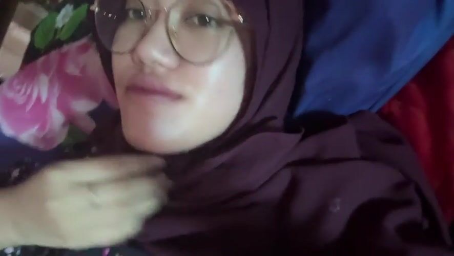 Woman in hijab photographed smiling on floral bedding