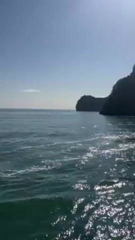 The video shows a boat traveling on the ocean with a view of islands in the background. The water is green and the sky is blue. The boat appears to be carrying cargo and has a green roof. A flag of Vietnam is flying on the boat.