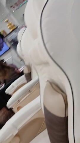 The camera pans upwards to capture the interior of a nail salon. A white pedicure chair dominates the foreground. The ceiling is black with rows of sparkling, crystal-like light fixtures. The walls are mirrored and display the name of the salon, "JENNY'S NAILS," in sparkly red letters. A large television screen shows a close-up of manicured hands. A nail polish display and other salon equipment are visible in the background. People can be seen in the background receiving services.