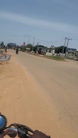 The video shows a person riding a motorcycle on a paved road. On the right side of the road, there is a building labeled "CICMA HOUSE," which is the "CHARTERED INSTITUTE OF COST AND MANAGEMENT ACCOUNTANTS (CIMA)." Farther down the road is a car dealership, “KAFADONA.” The sky is blue, and power lines run overhead.