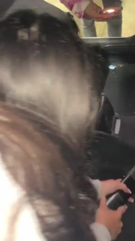 The video shows a person inside a car, potentially cleaning the car. A person can be seen outside the vehicle holding a light. The camera is angled towards the floor of the car, revealing dirt and debris. Someone's hand can be seen reaching down towards the floor, possibly to clean it.