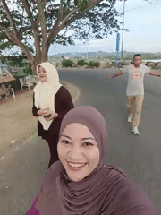 Three people walk on road, woman in hijab smiles