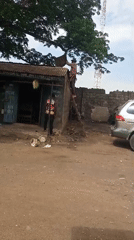 Man climbs wooden ladder onto dilapidated shop roof in rural Nigeria
