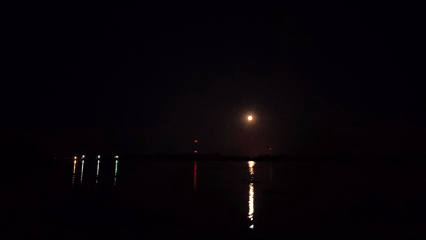 Full moon over a Russian waterway, red lights on the horizon