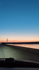 Car drives waterside road at dusk in Chaikovsky, Russia