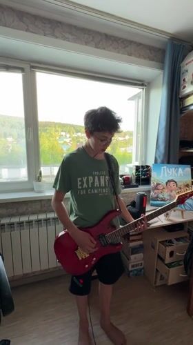 Boy plays red electric guitar indoors in Mezhdurechensk