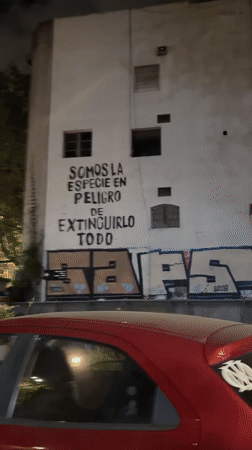 Motorcyclist rides past environmental graffiti in Buenos Aires at night