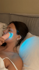 Woman uses light therapy facial device in bed