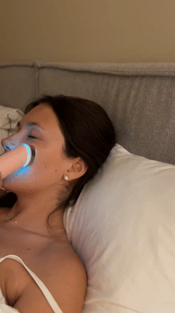 Woman uses light therapy facial device in bed