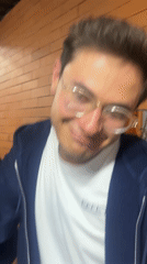 Man in glasses and blue jacket photographed near brick wall