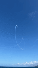 Aircraft performs aerobatic display with smoke trails over coastal waters