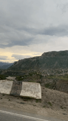 Car travels mountain road past village on cloudy day