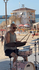 Street drummer performs on pink kit at busy Tel-Aviv beach