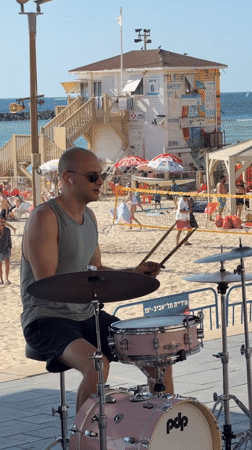 Street drummer performs on pink kit at busy Tel-Aviv beach