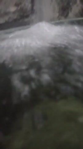A close-up vertical shot shows the surface of water as it is agitated, with small waves and bubbles forming. A dark green, possibly mossy, surface is visible beneath the water. The scene is dimly lit.