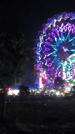 Nighttime carnival with illuminated Ferris wheels operates in Titibaro, Indonesia