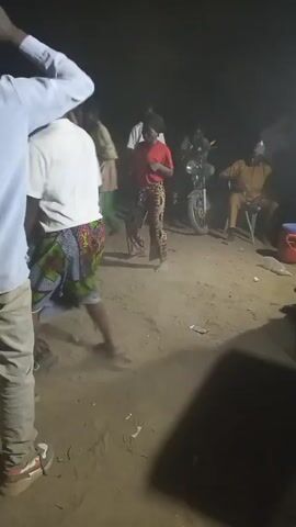 The video shows a group of people dancing in a sandy outdoor area at night. The lighting is dim, and there appears to be a motorcycle parked nearby. The group is of mixed gender and appear to be moving to music playing in the background.