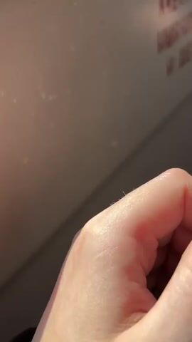 The video is a close-up shot of a person's hand wearing a silver ring with clear rectangular stones. The hand is illuminated by natural light, showing soft skin and manicured fingernails with a light pink polish. The background is a light-colored surface, possibly a wall, with blurry red text visible on the right side. Sparkles and light refractions are visible on the background, suggesting sunlight hitting a reflective surface. The hand moves slightly, allowing the viewer to see the ring from different angles.