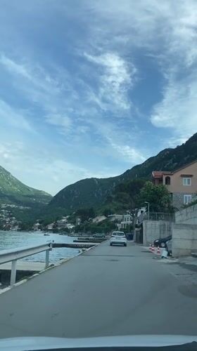 White car travels coastal road in Kotor, Montenegro
