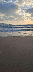 Afternoon at an urban beach with waves, sailboat, and city skyline