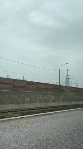 The video starts with a view from a moving car of a roadside barrier on a gray day, with power lines and towers visible beyond the barrier. The camera then pans towards the interior of the car, showing the seatbelt and a passenger. The camera moves to focus on the head of a black dog in the back seat. The dog's head is turned to the side and its mouth is open, with its tongue visible.
