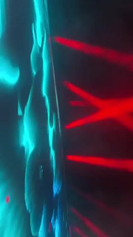 The video shows a close-up, side-view of a textured surface that is illuminated by both teal and red lights. The teal light is on the left side of the frame and creates a wavy, textured pattern on the surface. The red light is on the right side of the frame and appears as beams or streaks of light. The lighting creates a dynamic and abstract visual effect. The surface itself is not clearly identifiable but appears to be either a screen displaying graphics or a textured wall. The overall impression is one of an artistic lighting display, possibly in a nightclub or event setting. There are no discernible people or specific actions taking place.