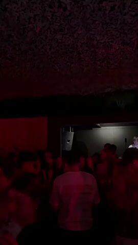 This video shows a crowded party scene. In the first few seconds, the camera is looking upwards at a dimly lit ceiling with red lights. The perspective then shifts to show a crowd of people dancing in a dark room illuminated by red lights. The scene transitions to an outdoor party at night with a pool. People are gathered around and in the pool, some dancing and socializing. The lighting appears to be a mix of colored lights and ambient darkness.
