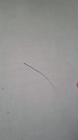 A close-up, medium-angle shot focuses on a person's hand and a single strand of dark hair. The hand, with visible fingernails and finger pads, is positioned on the right side of the frame, its index finger and thumb gently holding the hair strand. The hair appears thin and is curved, lying on a textured, light-colored surface, possibly a wall or paper. The background is predominantly this textured surface with a few faint, dark specks, possibly dust. The lighting is neutral, casting no harsh shadows and illuminating the scene evenly. The video is static, with no camera movement or discernible sound.