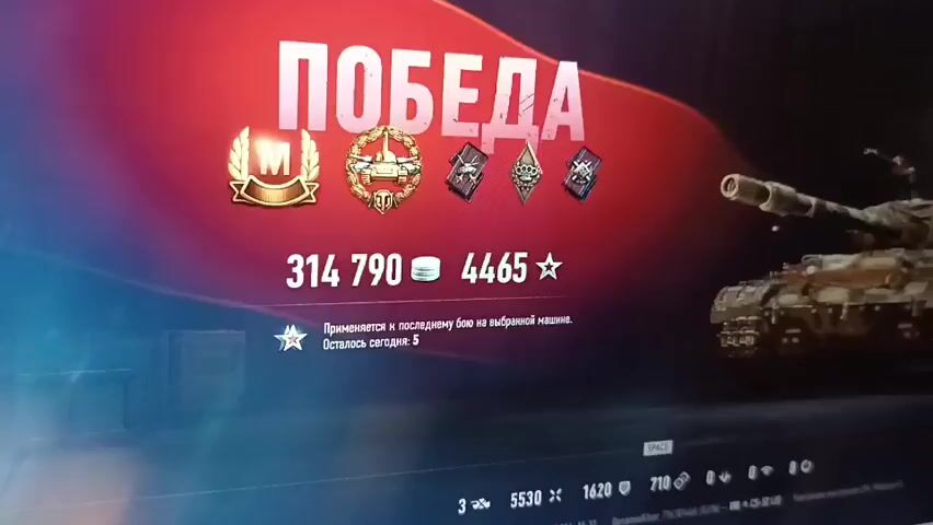 The video displays a "VICTORY" screen from a video game, likely World of Tanks, as indicated by the tank graphics and iconography. The screen shows several awards, including a gold medal with an "M" inside, a wreath with a tank in the center, and two diamond-shaped emblems. Below these awards are numerical values: 314,790, likely representing experience or credits earned, and 4465, probably signifying free experience or a similar game currency. There is also a note indicating that a bonus applies to the last battle on the selected machine, with 5 bonuses remaining for the day. A tank is visible on the right side of the screen. The bottom of the screen shows game statistics and what appears to be a timestamp.