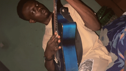 Young musician plays acoustic guitar on bed in Jos