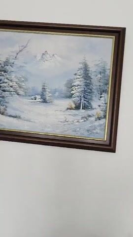 A point of view video depicts a pan from left to right of a white wall with several pictures hanging on it. The first picture shows a winter landscape with snow-covered trees and a river. The second picture shows a snow-covered landscape with a small house and a bright yellow sunrise. The third picture shows a snow-covered village with a bridge and a church. The fourth picture shows a black and gold poster of a 100-dollar bill, with Benjamin Franklin's face in gold and the rest of the bill in black and blue hues. The video ends with a partial view of another picture on the wall.
