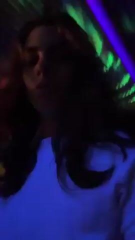 A person wearing a light-colored shirt and dark pants or shorts is shown in a dark environment. The lighting is dim, and there are neon lights in various colors on the floor, walls, and ceiling. The person walks along the floor, and the lights seem to respond to their movement. The lighting changes color frequently. The person's face is mostly obscured.