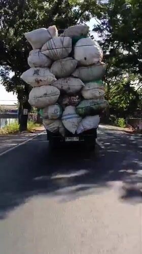 Heavily loaded pickup truck hauling white sacks through Panji Lor