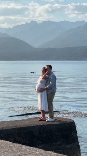 Couple embraces on a mountain-backed pier in Binda, Italy