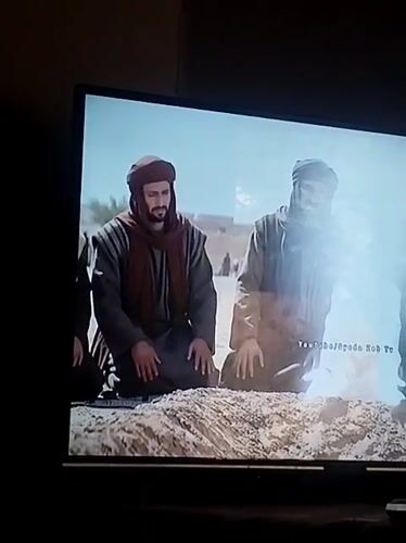 Three men kneel on sand in Dera Chahal, Pakistan